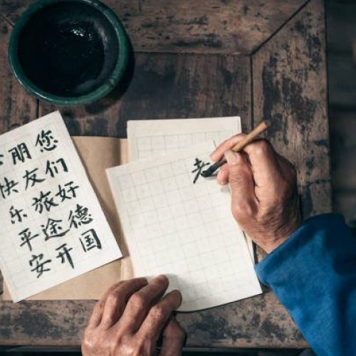close up of old hands writing chinese calligraphy characters with india ink on paper