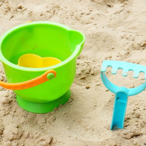 A plastic toy bucket and a blue sand rake on the sand